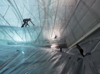 People climb on large inflated transparent sheets in an atrium space.