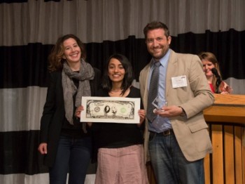 Three people pose with a large image of a $100 bll.