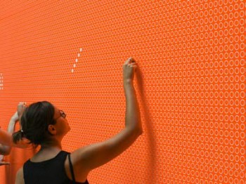 A person touches a bright orange wall with many small white circles on it.