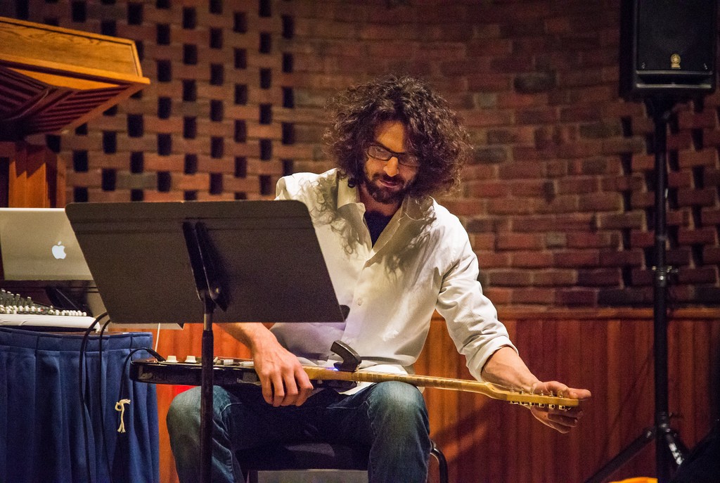 A man sitting at a music stand tunes a guitar.