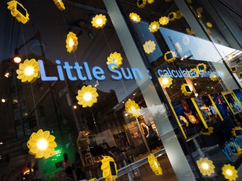 A window display showing hanging chains of sun-shaped lights reads "Little Sun: calculated simplicity"