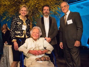 Four people pose for a photograph: three are standing and one is in a wheel chair.