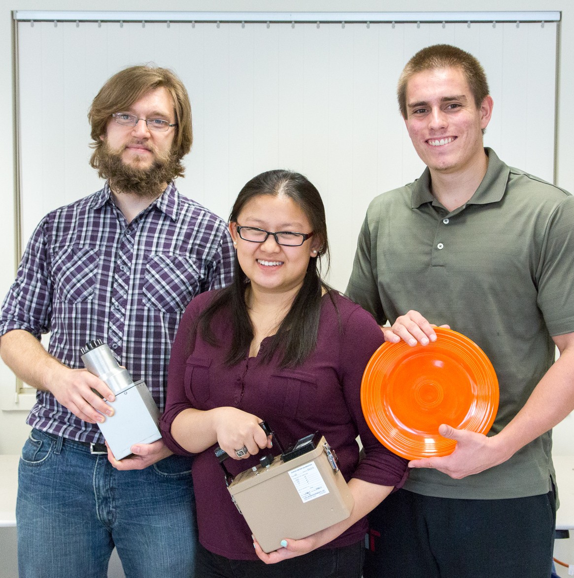 Three students pose holding metals and ceramic objects.