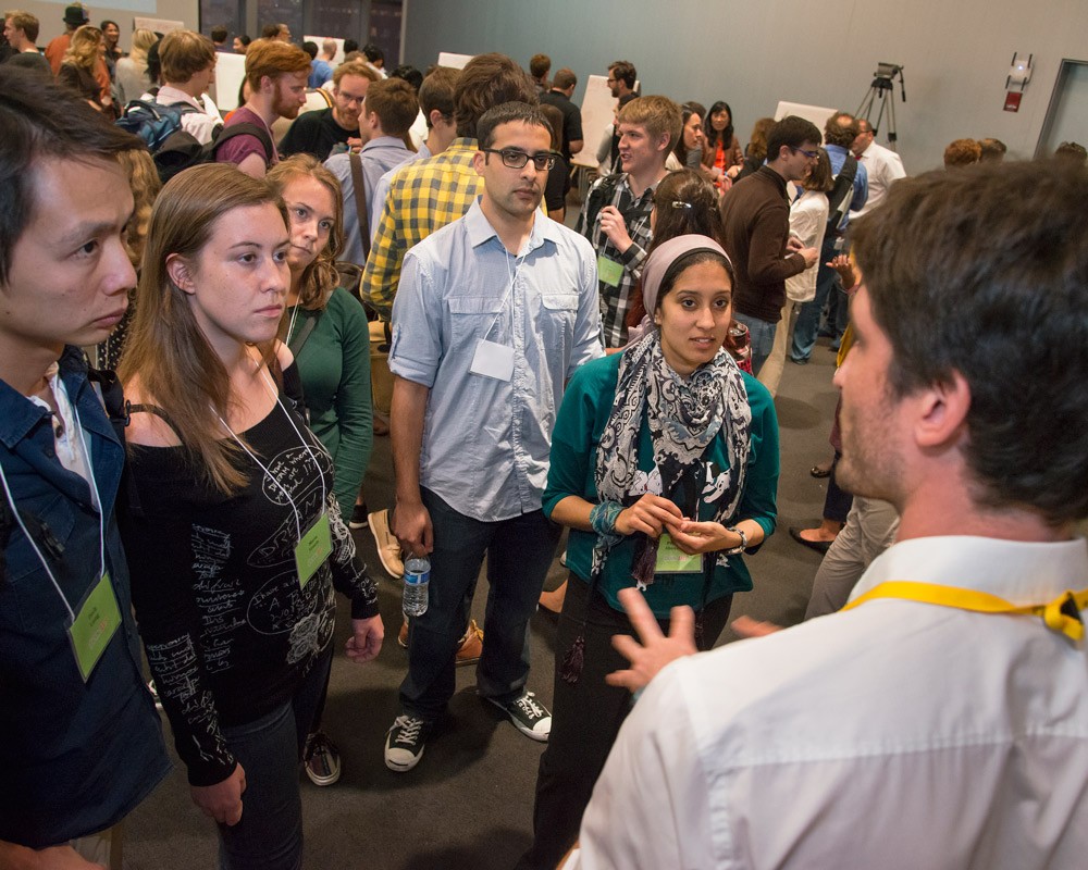 A man speaks to a group of five people at a busy event