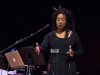 A woman moves her hands around an electronic device on a stage.