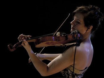 A woman performs violin against a black background