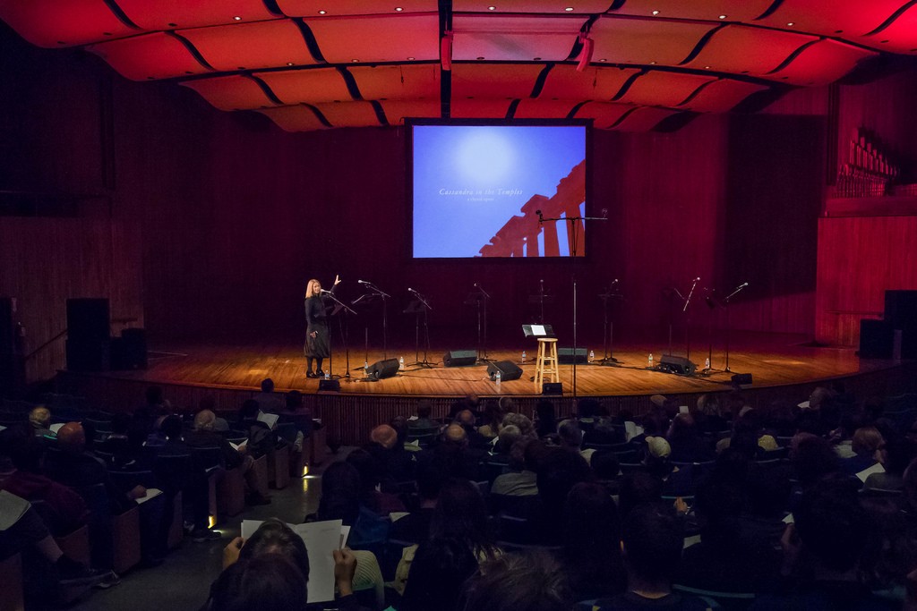 A speaker presents on a stage in a large auditorium.