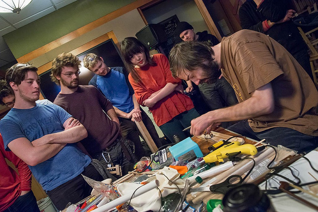 An artist builds an instrument while four students look on.