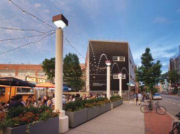 A sidewalk scene with a restaurant, flowers, and decorative lights.