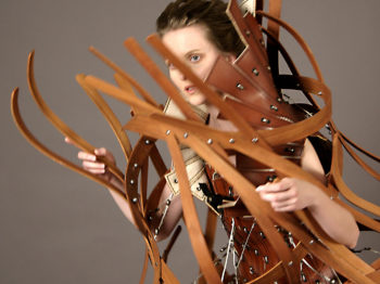 A woman wears a complex structure of thin wood pieces.