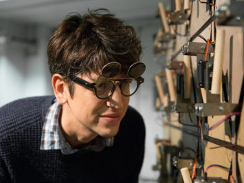 A student looks closely at a sculpture made of wood, metal, and wires.