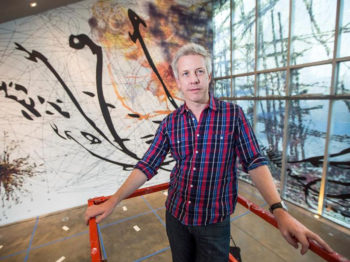 Artist standing in front of a large wall painting.