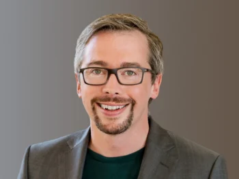 MIT Museum Director Michael John Gorman smiles at the camera in front of a grey background.