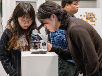 An MIT student looks into a microscope while another student looks on.