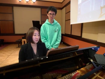 Mi-Eun Kim sits at the piano while student Holden Mui watches.