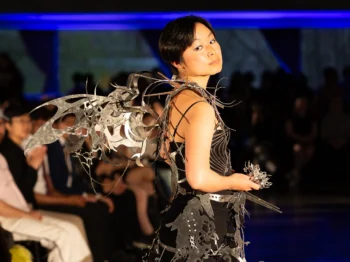 Model poses with a wing-like structure attached to the back of a black dress.