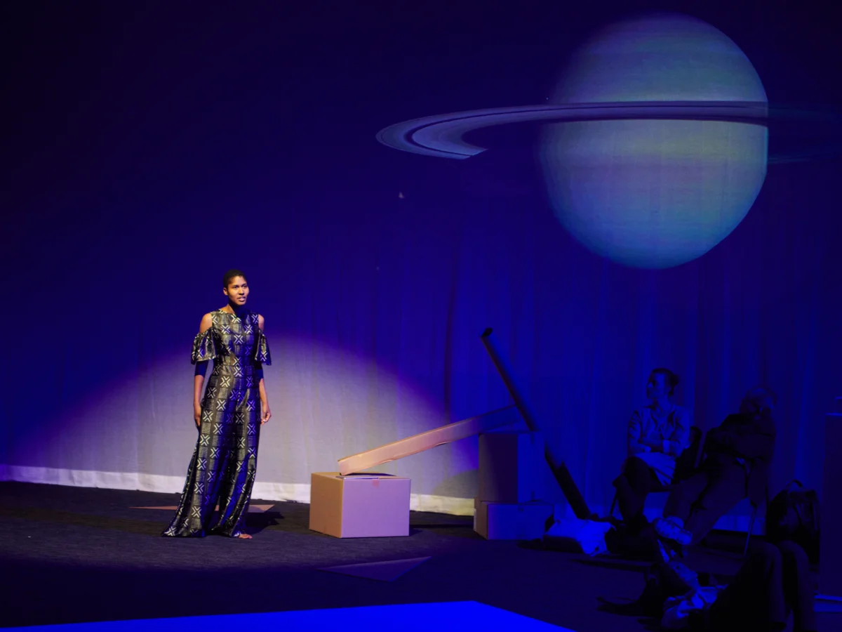 Woman on stage lighted in purple with image of Saturn